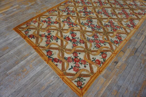Low-pile rug in cream with red roses and a yellow ribbon trellis pattern on distressed gray wood floors.