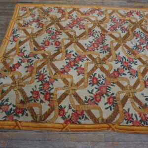 Low-pile floral rug with gold ribbon lattice and red flowers over weathered wooden flooring.
