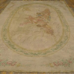 Faded cream rug displaying a central scene with figures, surrounded by pink roses, placed on a wood floor.