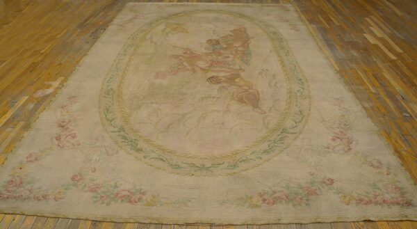 Faded cream rug displaying a central scene with figures, surrounded by pink roses, placed on a wood floor.