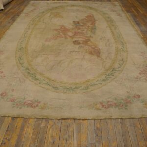Large, low-pile tan rug with faded classical figures and pink floral garlands on distressed wood planks.