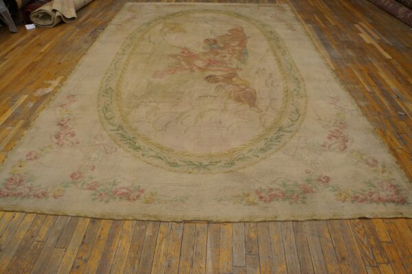 Large, low-pile tan rug with faded classical figures and pink floral garlands on distressed wood planks.