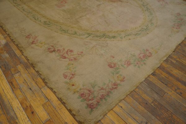 Shaggy beige rug with pink and green floral borders lies diagonally across worn wood flooring.