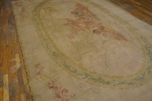 Large beige rug featuring a faded central oval medallion with figures and floral borders on wood flooring.
