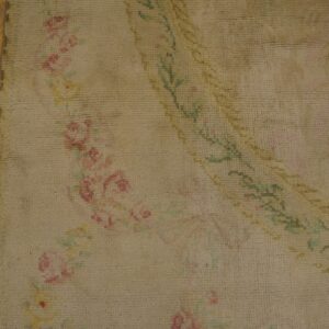 Close-up of a beige rug featuring faded pink and green floral designs next to rustic wood floorboards.