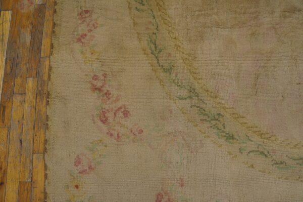 Close-up of a beige rug featuring faded pink and green floral designs next to rustic wood floorboards.