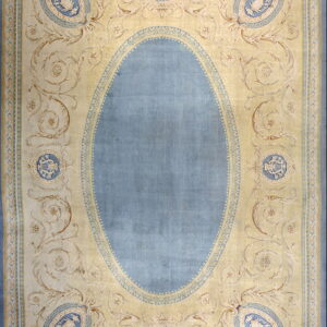 Pale yellow rug with a solid blue central oval and elaborate scrollwork featuring blue classical medallions.