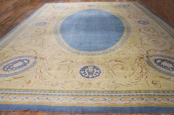 Large blue medallion rug on a cream and yellow field with detailed scrollwork borders over wood flooring.