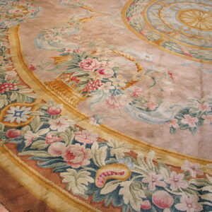 A close-up of a low-pile mauve rug displaying an elaborate pink and green floral border and central blue and gold medallion.