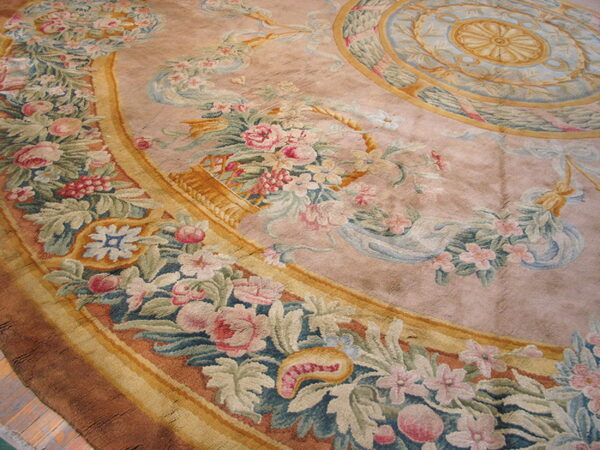 A close-up of a low-pile mauve rug displaying an elaborate pink and green floral border and central blue and gold medallion.