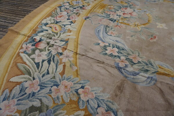Distressed low-pile rug detail showing pastel floral garlands, a yellow border, and a taupe field on wood flooring.