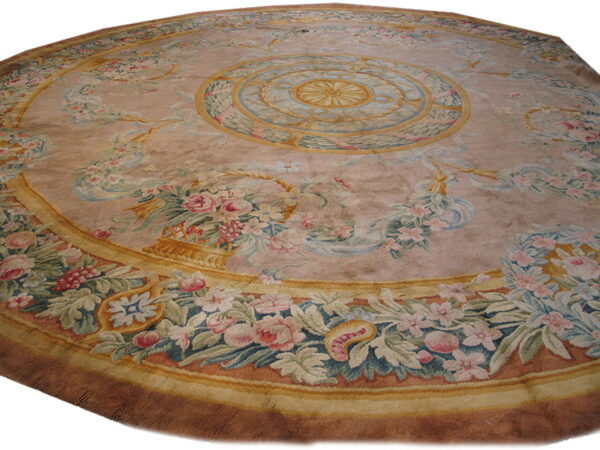 Ornate round low-pile rug with a dusty pink field, yellow borders, and blue, pink, and green floral designs.