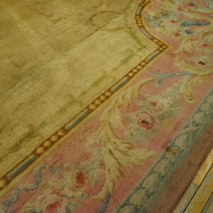 A gold rug with a dusty pink and blue floral border rests on distressed yellow wooden planks.