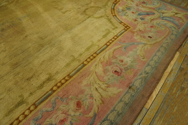 A gold rug with a dusty pink and blue floral border rests on distressed yellow wooden planks.