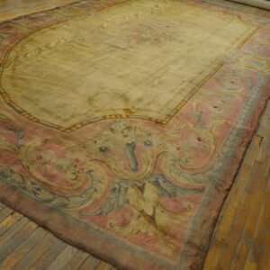 Ornate floral rug in muted yellow, pink, and blue, lying on worn wood plank flooring.