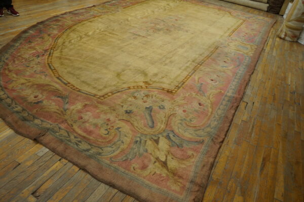 Ornate floral rug in muted yellow, pink, and blue, lying on worn wood plank flooring.