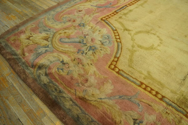 High-pile rug with a pale yellow field and ornate border in pink, blue, and gold on wooden floor.