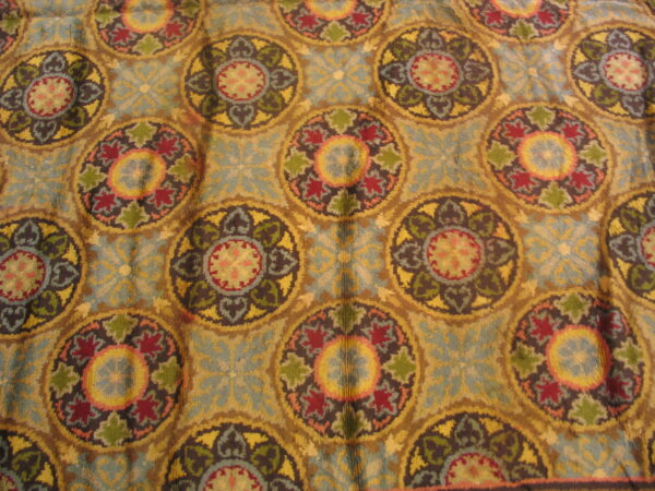 Repeating distressed medallion pattern rug in faded teal, gold, burgundy, and olive green colors.