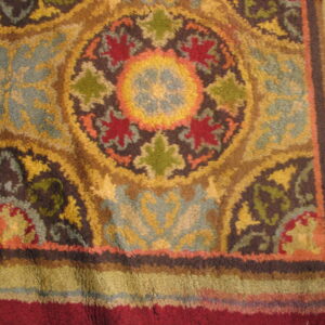 Close-up of a high-pile rug detail featuring ornate floral medallions in gold, red, dusty blue, and green.