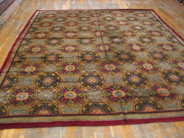 Large rug with repeating colorful medallions and a prominent red border on worn wooden floors.