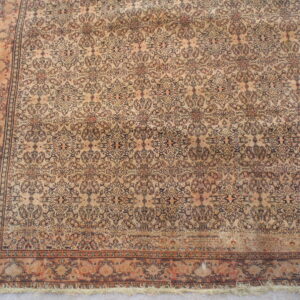 Distressed beige rug featuring a complex repeating floral pattern in dark brown and faded orange on concrete.