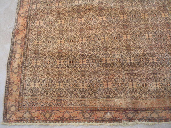 Distressed beige rug featuring a complex repeating floral pattern in dark brown and faded orange on concrete.