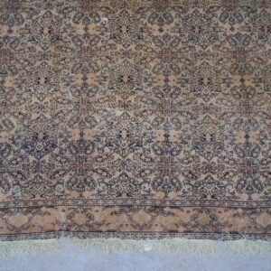 Distressed cream and navy rug with intricate patterns and fringe, displayed on a light gray floor.
