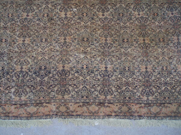 Distressed cream and navy rug with intricate patterns and fringe, displayed on a light gray floor.