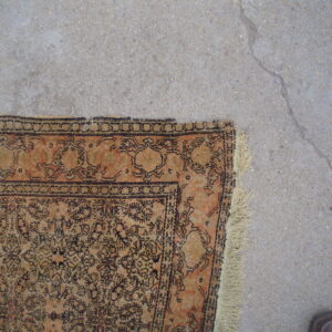 A distressed orange and tan patterned rug with dark motifs rests on cracked gray concrete flooring.