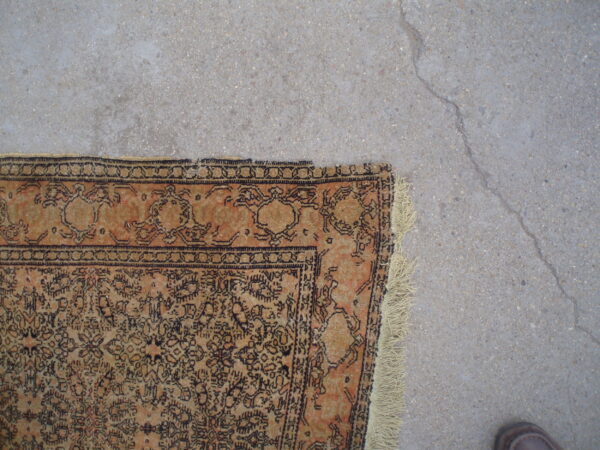 A distressed orange and tan patterned rug with dark motifs rests on cracked gray concrete flooring.