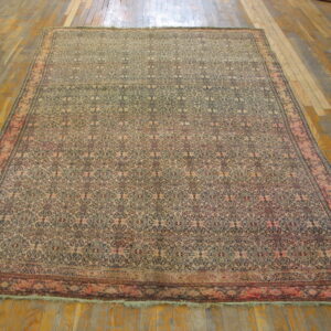 Beige and navy patterned low-pile rug with pink borders rests on a wide plank wooden floor.