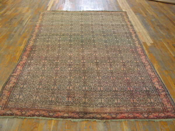 Beige and navy patterned low-pile rug with pink borders rests on a wide plank wooden floor.