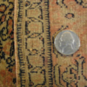 Muted orange and gold patterned rug detail with a dark border design and a silver quarter coin.
