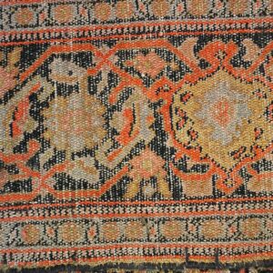 Detailed view of a low-pile rug featuring orange, gold, and black patterns overlapping a darker geometric rug.