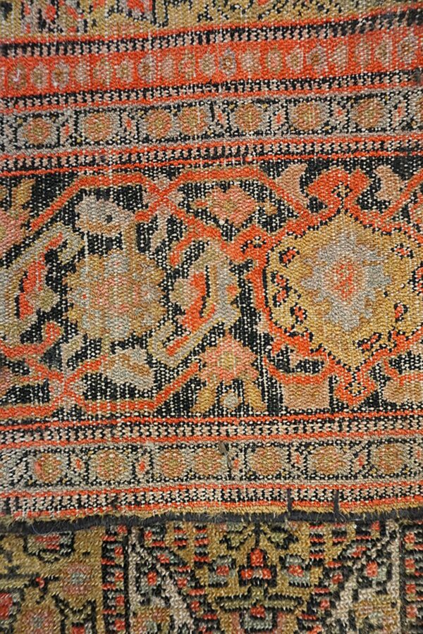 Detailed view of a low-pile rug featuring orange, gold, and black patterns overlapping a darker geometric rug.