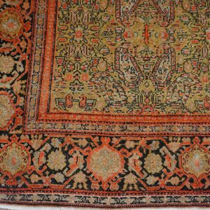 Low-pile rug corner showing detailed yellow field and bold red-orange and black borders on wood.