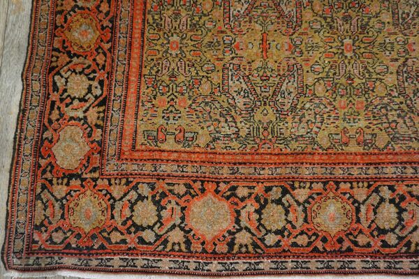 Low-pile rug corner showing detailed yellow field and bold red-orange and black borders on wood.