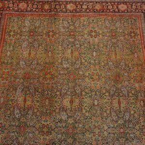 A detailed, low-pile rug featuring a complex all-over pattern in olive green, rust, and black on distressed wood floors.