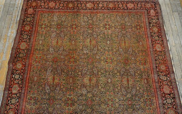 A detailed, low-pile rug featuring a complex all-over pattern in olive green, rust, and black on distressed wood floors.