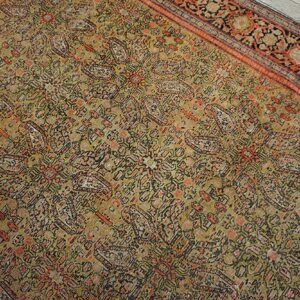 Muted olive rug with dense floral pattern and rust-red border resting on light gray wood flooring.