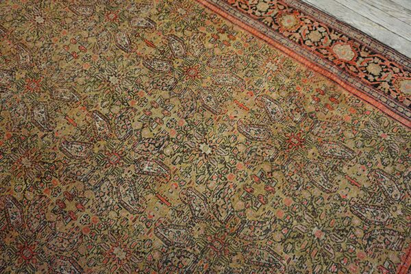 Muted olive rug with dense floral pattern and rust-red border resting on light gray wood flooring.