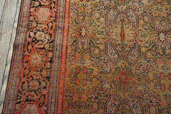 Intricate traditional rug pattern in mustard, black, and rust colors against distressed gray wood planks.