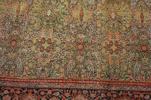 Low-pile rug with geometric patterns in faded olive, gold, red, black, and multiple borders.