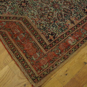 Close-up of a densely patterned rug corner in red, black, and muted tan resting on hardwood flooring.