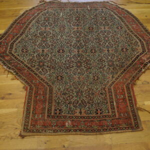 Polygonal rug with detailed red, dark green, and beige floral patterns on a wide plank wood floor.