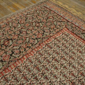 A muted traditional rug with red, slate, and dark brown patterns lies folded on rustic wood planks.