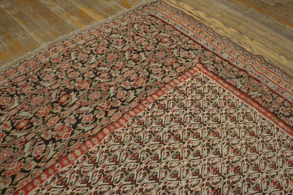 A muted traditional rug with red, slate, and dark brown patterns lies folded on rustic wood planks.