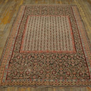 Dense traditional rug pattern in red, cream, and dark tones displayed on distressed wooden plank flooring.