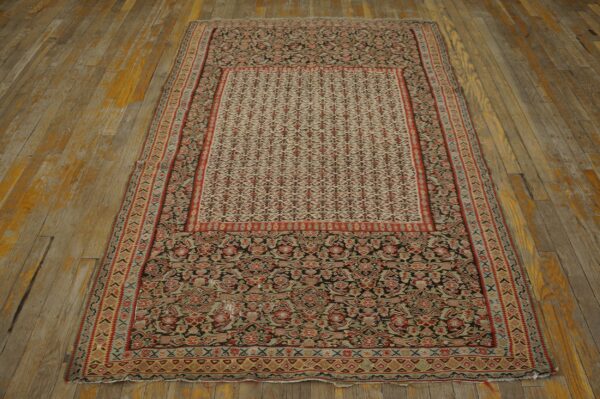Dense traditional rug pattern in red, cream, and dark tones displayed on distressed wooden plank flooring.