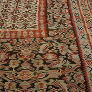 Geometric rug in faded red, black, and cream with teal accents lying on distressed wood flooring.